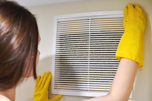A woman cleaning an air vent in a home.